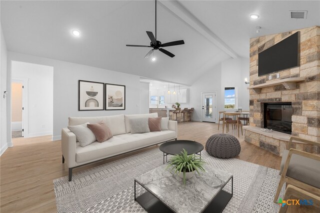 living room with a fireplace, light hardwood / wood-style floors, beamed ceiling, and ceiling fan