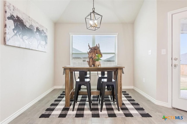 dining room with hardwood / wood-style flooring, vaulted ceiling, and an inviting chandelier