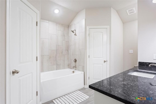 bathroom with vanity, lofted ceiling, and tiled shower / bath