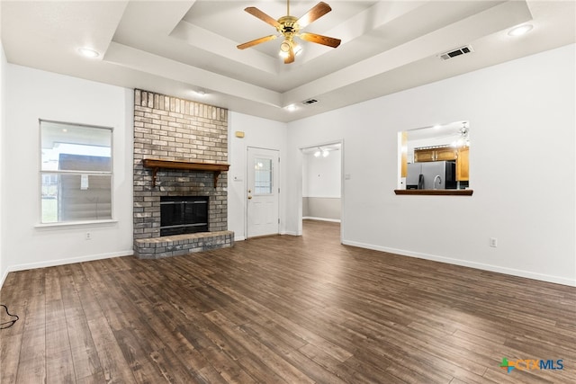 unfurnished living room with a tray ceiling, a ceiling fan, wood finished floors, and a fireplace