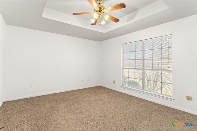 empty room with baseboards, a raised ceiling, ceiling fan, and carpet flooring