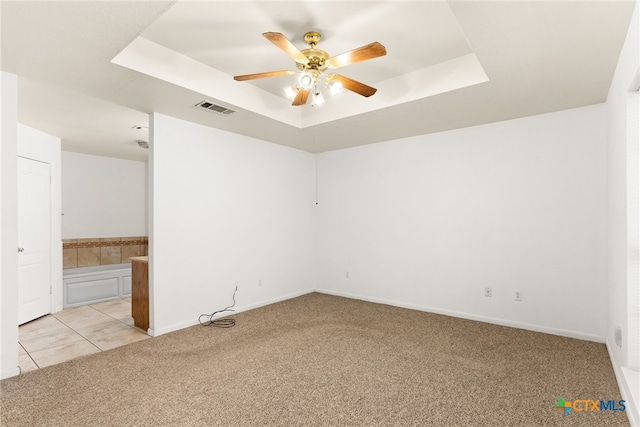 spare room with visible vents, light carpet, a ceiling fan, a tray ceiling, and baseboards