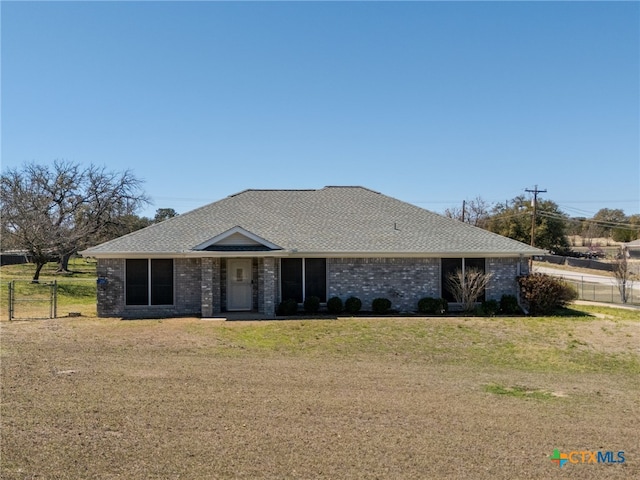 view of front of property with brick siding, roof with shingles, a front yard, and fence