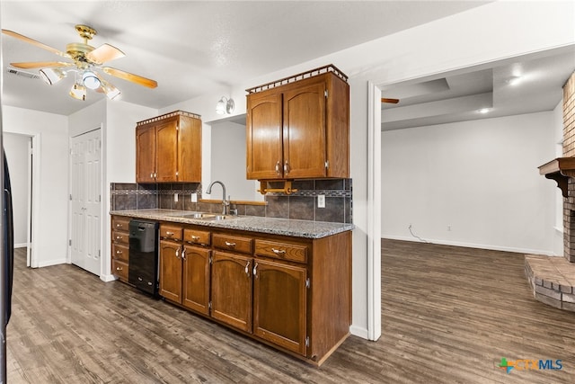 kitchen featuring visible vents, a sink, black dishwasher, brown cabinetry, and a fireplace