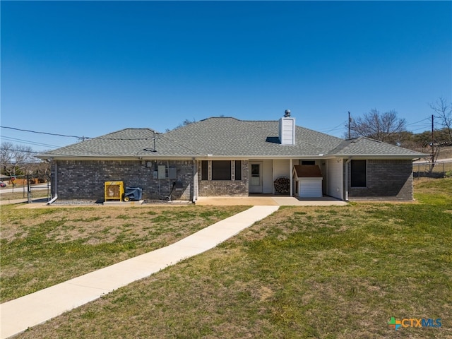 view of front of house with brick siding, a chimney, a front yard, and a shingled roof