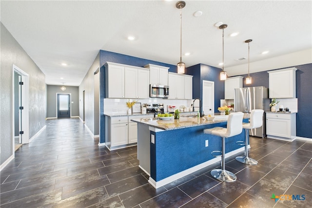 kitchen with stainless steel appliances, a sink, a center island with sink, decorative backsplash, and light stone countertops