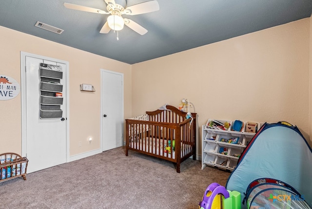 bedroom featuring a nursery area, ceiling fan, and carpet floors