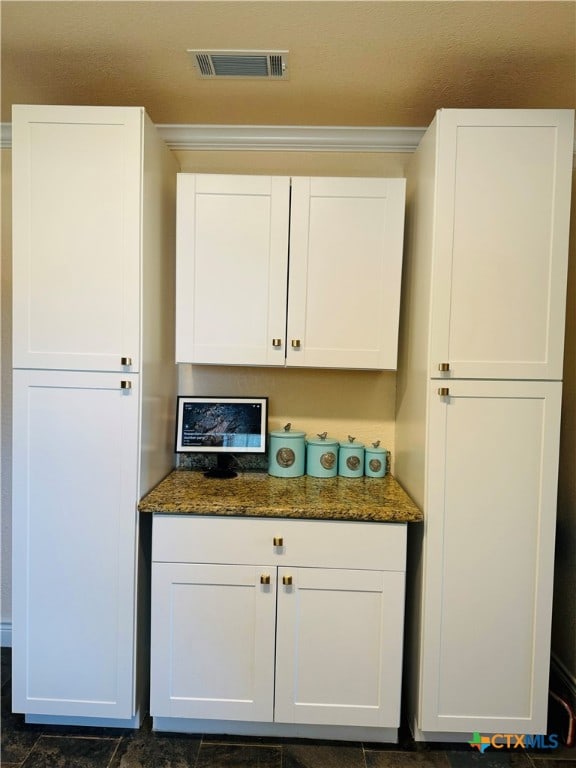 interior space featuring white cabinets, dark stone countertops, and crown molding