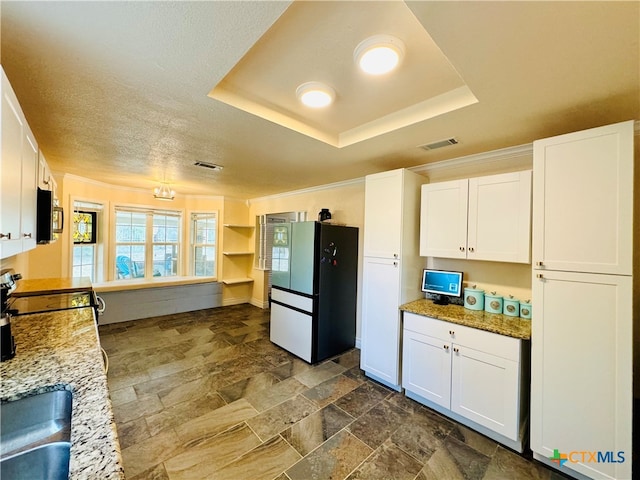 kitchen featuring light stone counters, range, a raised ceiling, white fridge, and white cabinetry