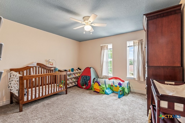 bedroom with a textured ceiling, light carpet, ceiling fan, and a crib