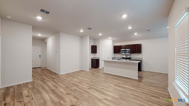 kitchen featuring light wood-type flooring, stainless steel appliances, light stone counters, and an island with sink