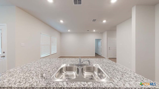 kitchen featuring light stone countertops, a center island with sink, sink, and light hardwood / wood-style flooring