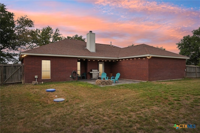 back house at dusk featuring a patio area, a yard, and a fire pit