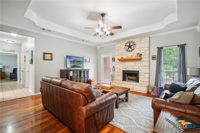 living room featuring wood-type flooring, ornamental molding, ceiling fan, a raised ceiling, and a fireplace