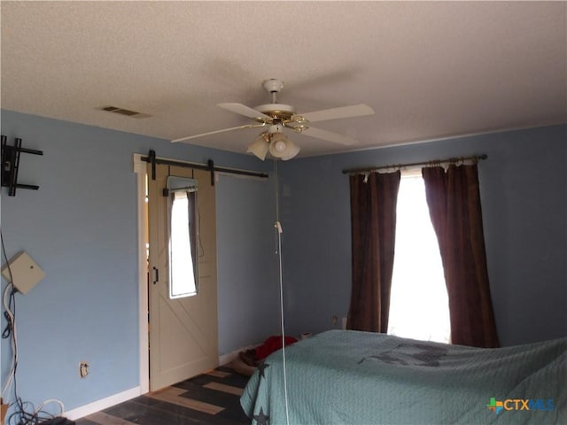 bedroom with a textured ceiling, a barn door, a ceiling fan, visible vents, and baseboards