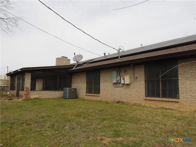 view of property exterior featuring solar panels, brick siding, a sunroom, a yard, and a chimney