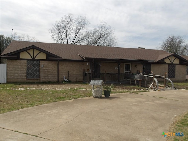 view of front facade with covered porch, a shingled roof, concrete driveway, and brick siding