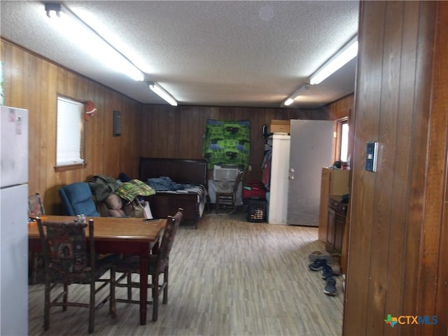 dining space with wood walls, light wood-style flooring, and a textured ceiling