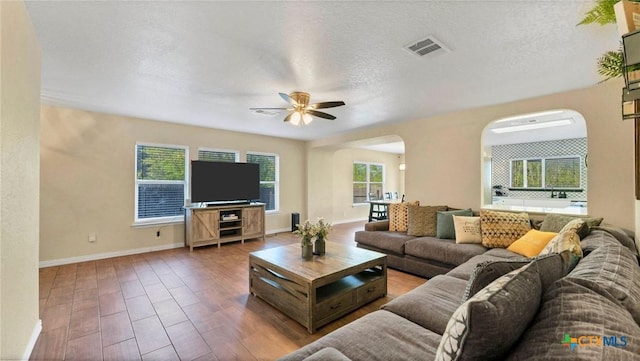 living room with arched walkways, ceiling fan, baseboards, wood finished floors, and a textured ceiling