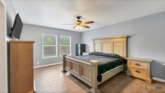 bedroom with a textured ceiling, baseboards, wood finished floors, and a ceiling fan