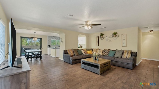 living room with arched walkways, dark wood-type flooring, a ceiling fan, and baseboards