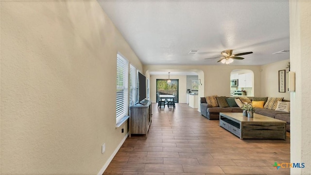 living room featuring arched walkways, ceiling fan, wood finished floors, and baseboards