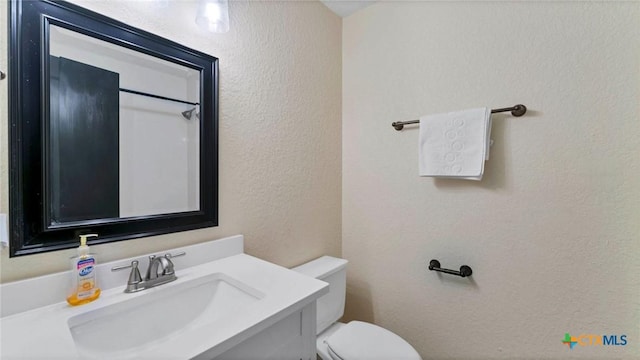 bathroom featuring toilet, a textured wall, and vanity
