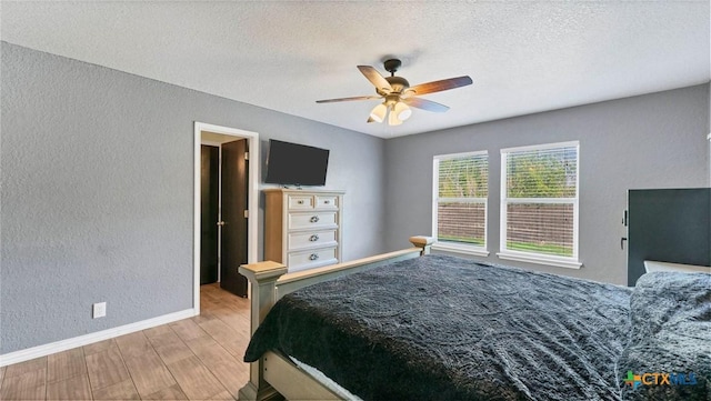bedroom with a textured wall, wood finished floors, baseboards, a textured ceiling, and a ceiling fan