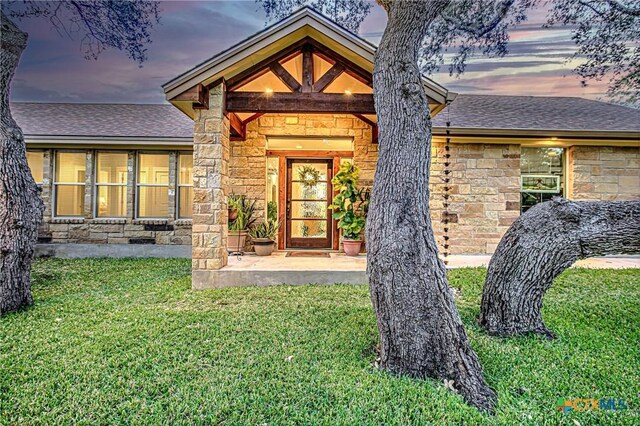 1002 Merry Ln, Kingsland, TX 78639 - exterior entry at dusk featuring stone siding, a lawn, and a shingled roof