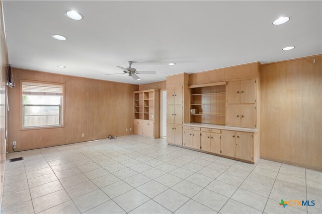 unfurnished living room with wood walls, light tile patterned flooring, and ceiling fan