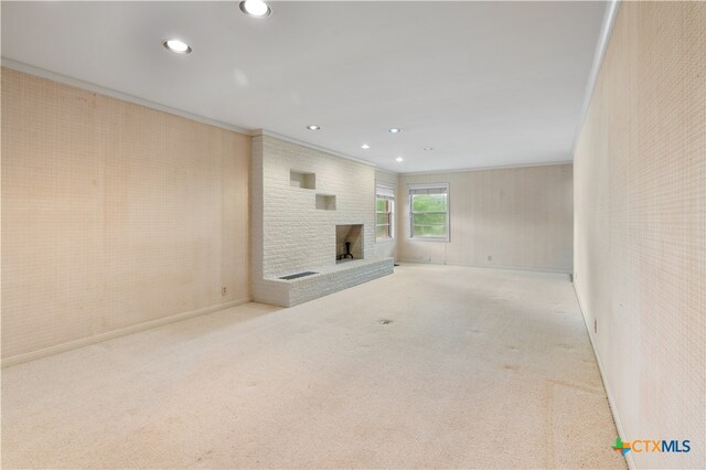 unfurnished living room featuring a brick fireplace, light colored carpet, and crown molding