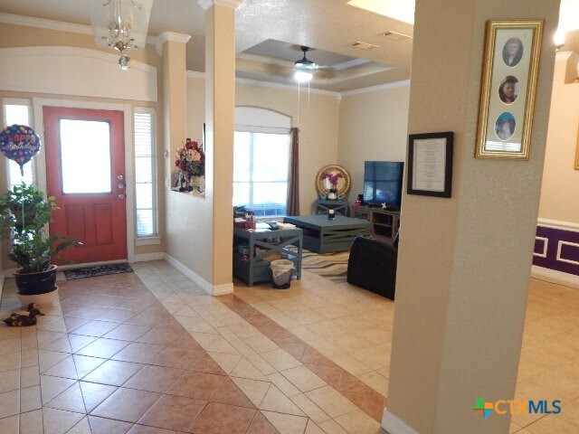 entrance foyer featuring crown molding, light tile patterned floors, ornate columns, a tray ceiling, and ceiling fan with notable chandelier