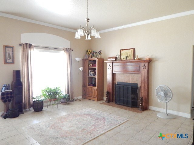 tiled living room featuring a tiled fireplace, crown molding, and an inviting chandelier