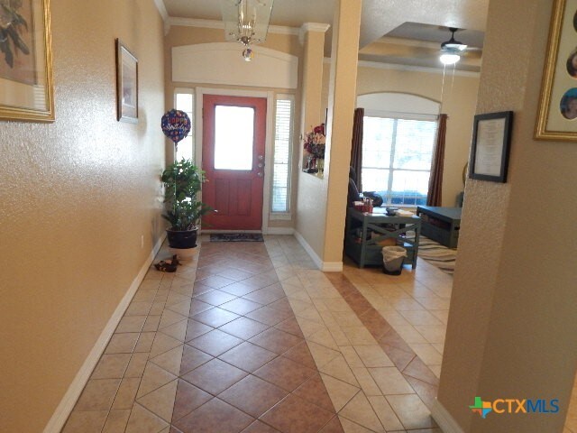 tiled entryway with ceiling fan with notable chandelier and crown molding