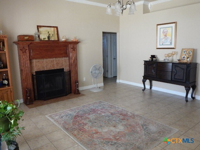 living room with a tiled fireplace, a chandelier, light tile patterned floors, and crown molding