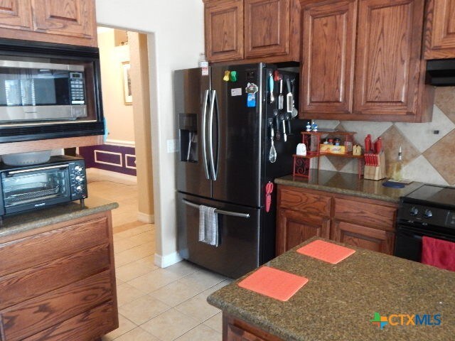 kitchen with stainless steel appliances, dark stone countertops, light tile patterned floors, backsplash, and ventilation hood