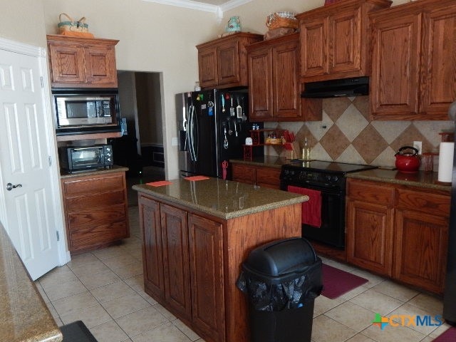 kitchen with black appliances, ornamental molding, light tile patterned flooring, a kitchen island, and backsplash