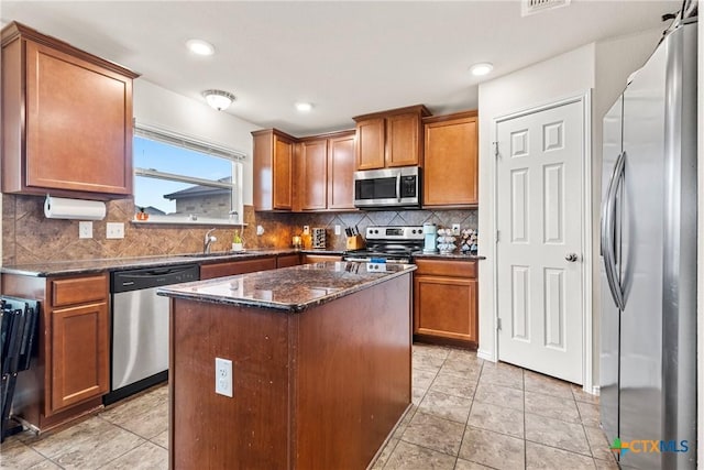 kitchen featuring dark stone counters, decorative backsplash, stainless steel appliances, brown cabinets, and a sink