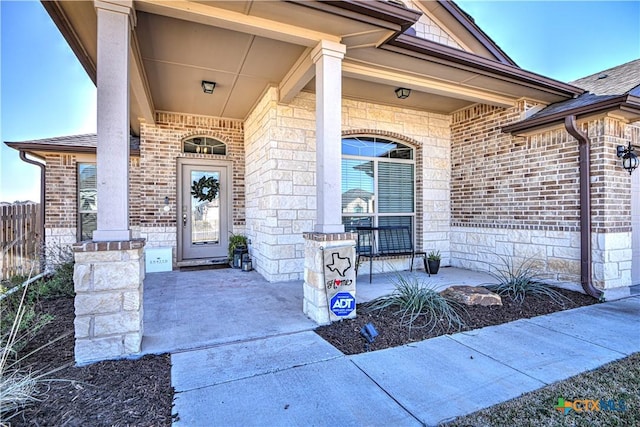 doorway to property featuring stone siding, brick siding, a porch, and fence