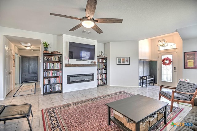 living area featuring visible vents, a textured ceiling, a glass covered fireplace, light tile patterned flooring, and ceiling fan