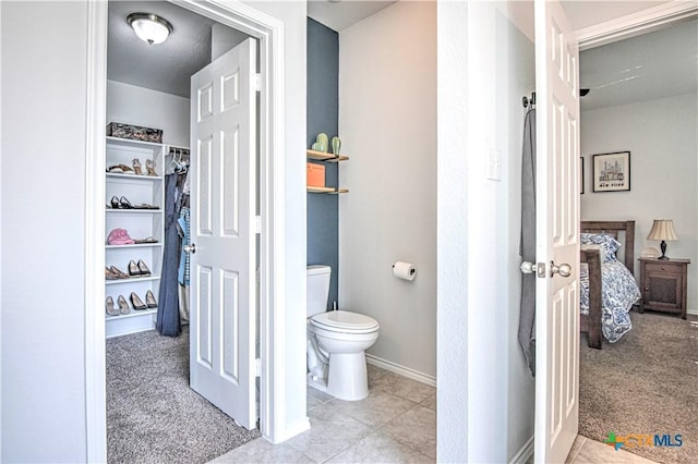 bathroom featuring a walk in closet, toilet, connected bathroom, tile patterned flooring, and baseboards