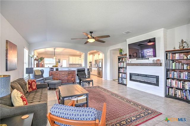 living room with arched walkways, visible vents, ceiling fan, and a glass covered fireplace