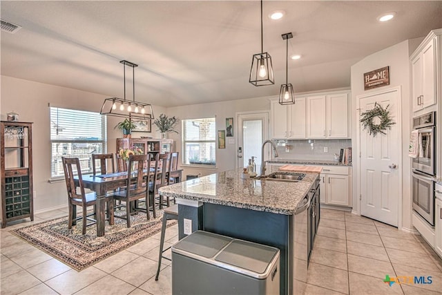 kitchen with a sink, backsplash, an island with sink, and white cabinetry