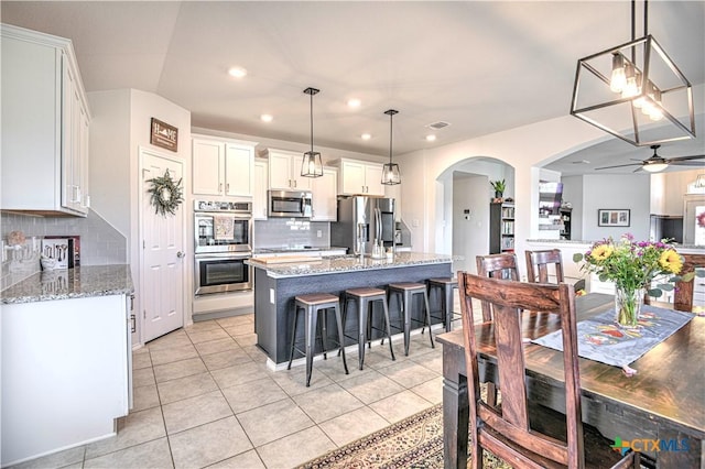 kitchen with a breakfast bar area, a ceiling fan, arched walkways, stainless steel appliances, and white cabinets