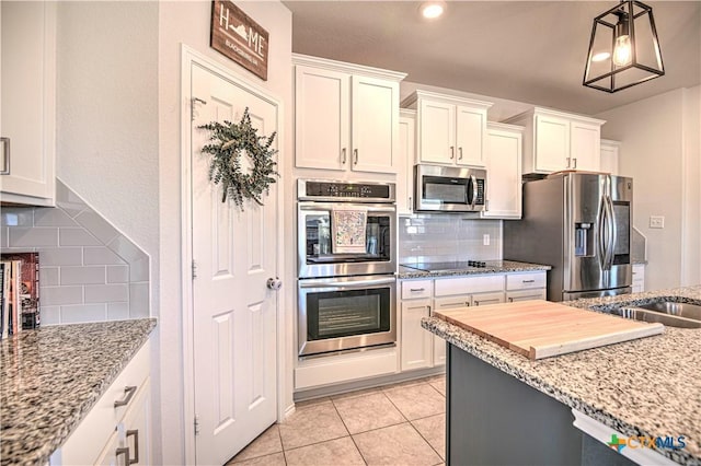 kitchen with light tile patterned floors, light stone countertops, stainless steel appliances, decorative backsplash, and white cabinetry