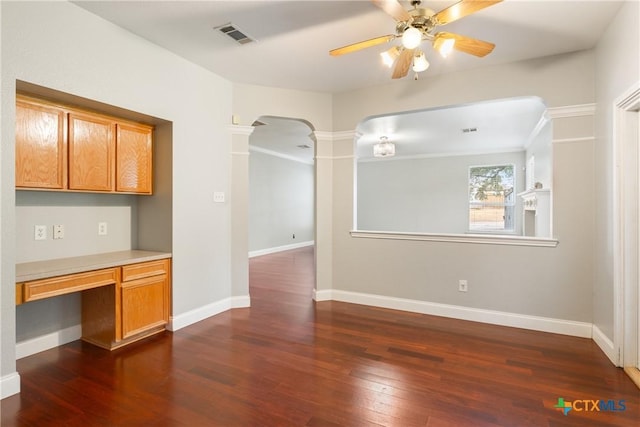 unfurnished dining area with ceiling fan, built in desk, dark hardwood / wood-style flooring, and ornate columns