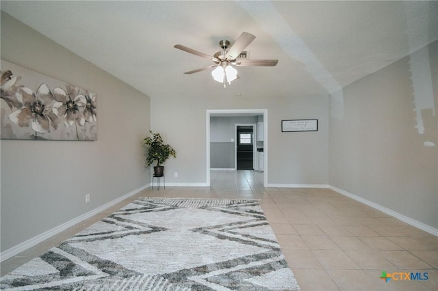 tiled empty room featuring baseboards and a ceiling fan