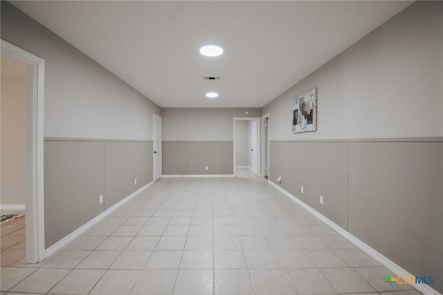 empty room featuring light tile patterned floors, wainscoting, and visible vents