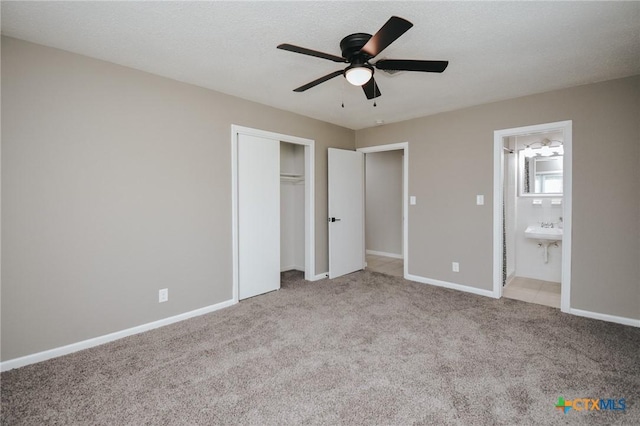 unfurnished bedroom featuring ceiling fan, baseboards, a closet, carpet, and ensuite bath