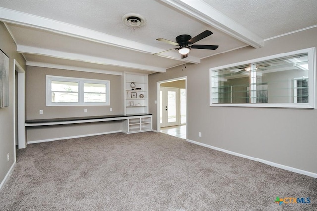 carpeted empty room with baseboards, a textured ceiling, ceiling fan, and beam ceiling